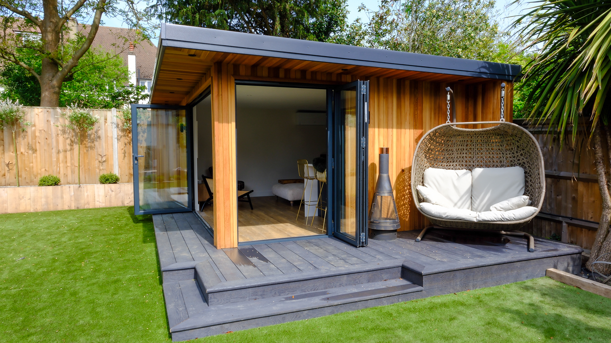 Small wooden garden room with black deck and comfy two-seater outside