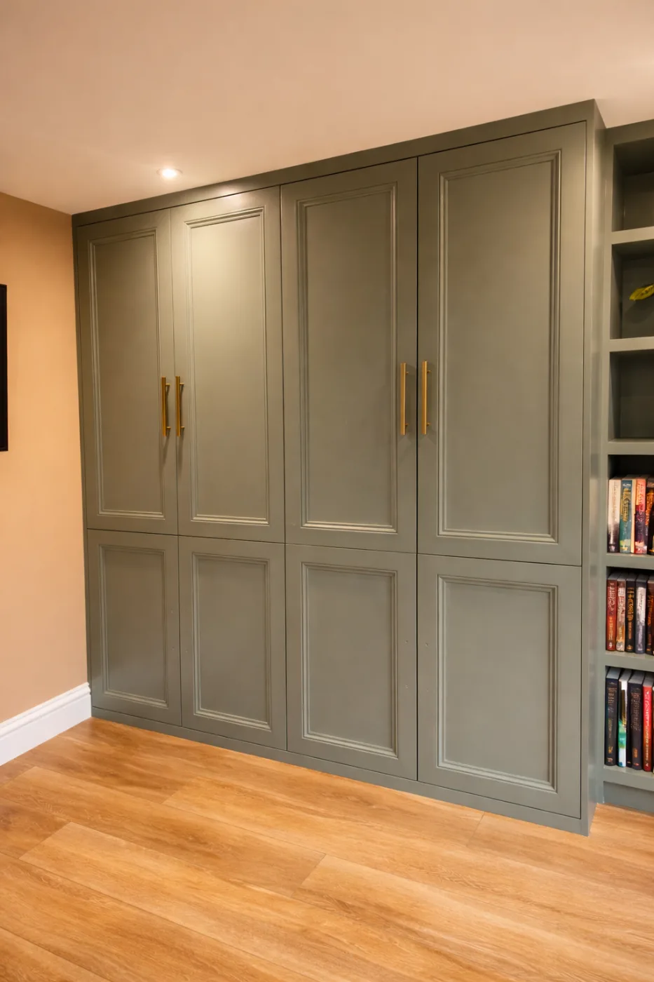 Painted built-in wardrobe doors with brass handles alongside integrated bookshelves